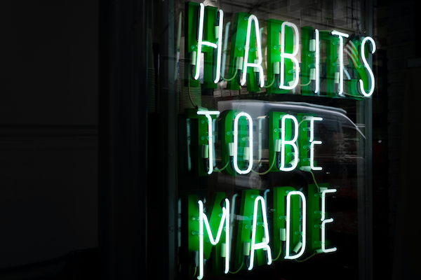Neon sign showing words "Habits to be made" in all capital letters in green against a black background